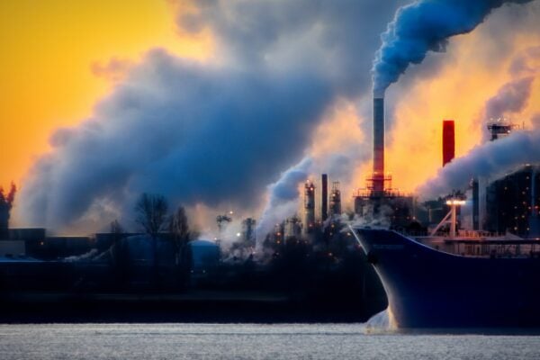 closeup of large ships with factory in background emitting smoke